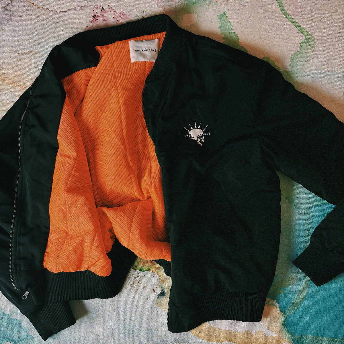 Black jacket with orange lining and DNO Skull embroidery on a textured surface. 
